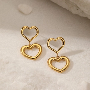 Detailed view of gold 18K plated stainless steel double heart drop earrings on white sand