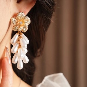 Gros plan de boucles d'oreilles fleurs dorées avec glands de perles blanches