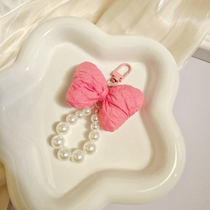 Detail of pink fabric bow keychain with white pearls on a decorative white cloud tray
