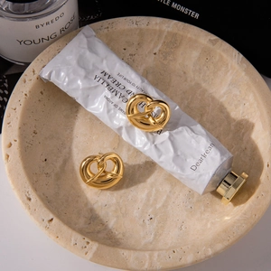 Detail view of gold-plated twisted pretzel stud earrings on a minimalist marble tray