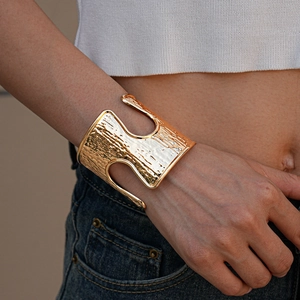 Detail of gold wide cuff bracelet with hammer texture and irregular hollow patterns