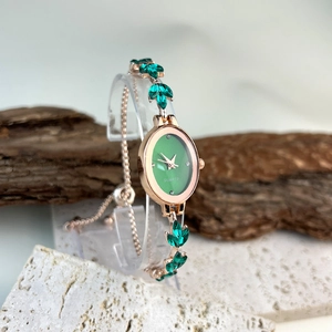 Detailed macro of oval quartz watch with rose gold finish and green leaf gemstone strap