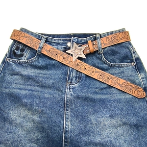 Vintage brown leather belt with rose embossing and a large silver star buckle on jeans