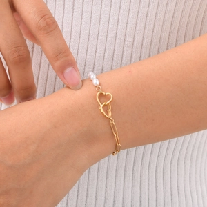 Detailed macro of gold heart-shaped charms and white pearl bracelet on a woman wrist
