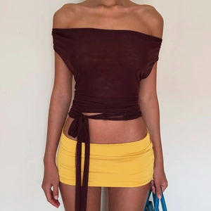 Détail du haut dos nu marron foncé avec lien à la taille et mini-jupe jaune sur modèle
