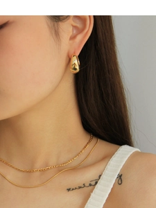 Close-up of stylish golden water drop hoop earrings and layered necklaces on a model