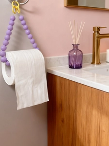 Detail of a purple beaded toilet paper holder hanging in a stylish bathroom setting
