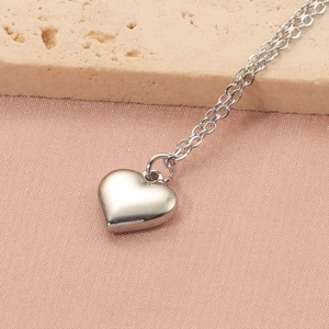 Gros plan détaillé du pendentif coeur poli sur une fine chaîne en acier inoxydable