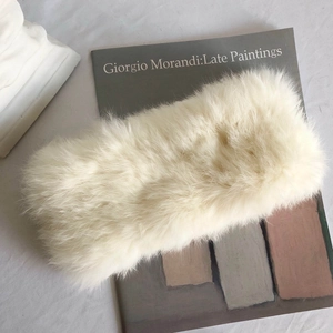 Weißes Kaninchenfell-Stirnband mit Plüschstruktur auf einem Buch in minimalistischem Stil