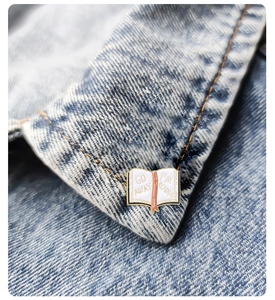 Detail of a book-shaped enamel pin on denim reading 'GO AWAY I'M READING'