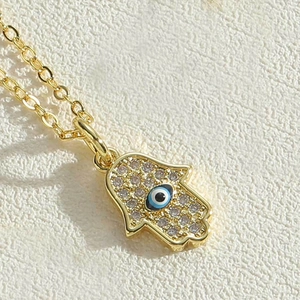 Close-up of golden Hamsa hand pendant with sparkling zircons and blue evil eye detail