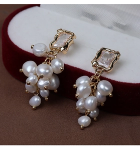 Macro view of gold-plated grape earrings with baroque pearls and zircon stones on velvet