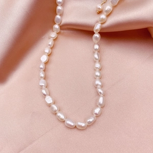 Close-up of baroque pearl necklace with gold clasp on pink silk background