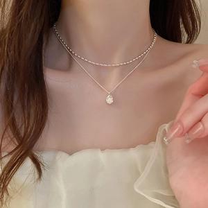 Detail of a double-layered silver pearl necklace with oval pendant on a model