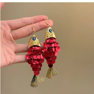 Detail of gold fish tassel earrings with red sequins and blue evil eye charms