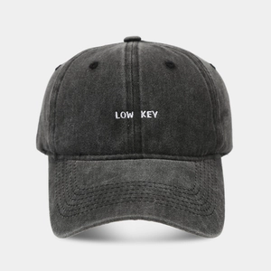 Close-up of white LOW KEY embroidery on a vintage washed grey cotton baseball cap