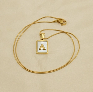 Détail du pendentif carré doré avec nacre blanche et lettre A sur chaîne serpent fine
