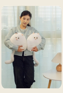 Detail of plush white Persian cat pillows held by a model in a cozy home setting