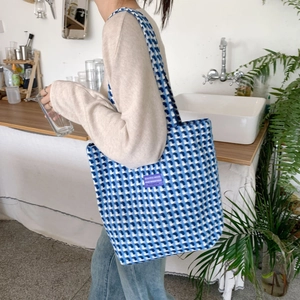 Blue and white plaid woven tote bag with a purple label shown on a shoulder