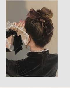Detail of velvet bow hair scrunchies in brown, beige, and black with small pearl accents