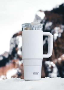 White TYESO 40oz insulated tumbler with wide handle and clear lid on outdoor snow background