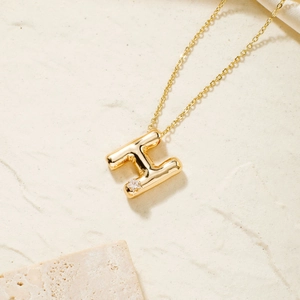Close-up of golden bubble letter H pendant with star-shaped zircon on textured stone backdrop