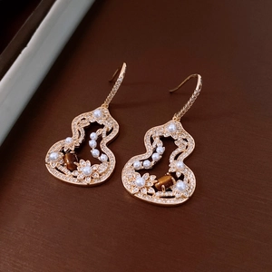 Macro shot of gold hollow gourd earrings with tiger eye stone and small pearls