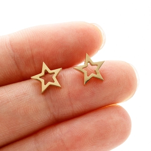 Macro shot of gold hollow star stud earrings on fingertips showing small size and detail