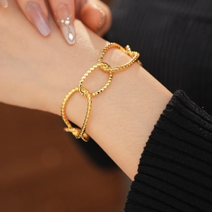 Close-up of gold-plated oval link bracelet with beaded texture on a model wrist