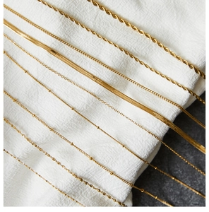 Detail showing multiple styles of gold plated stainless steel chains on white fabric