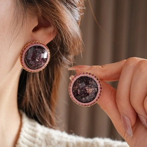 Macro detail of round resin earrings with purple gemstone, gold flakes and pink crystals