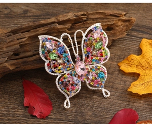 Gros plan d'une broche papillon vintage avec strass colorés posée sur une branche de bois