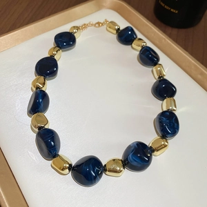Detail of deep blue resin beads and golden metallic spheres on an acrylic collar necklace