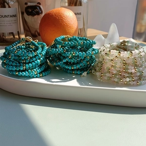 Multi-layer beaded bracelet with green turquoise and gold beads on a white plate