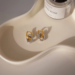 Macro shot of interlocking gold and silver oval hoop earrings on cream ceramic tray