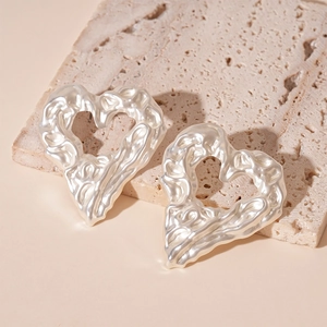 Detailed view of silver heart earrings with wrinkled metal texture on a stone base