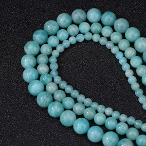Natural blue-green Amazonite round beads arranged in curved strings on dark background