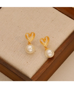 Macro shot of gold hollow heart earrings featuring round white pearl drops on fabric