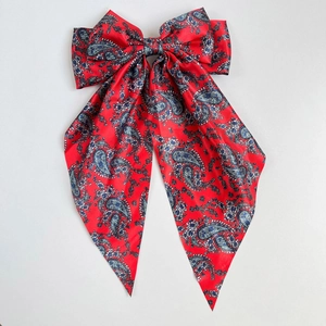 Detailed macro of red paisley print satin hair bow clip showing glossy silk texture