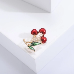 Elegant red cherry brooch with golden finish on a white geometric display stand