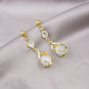 Macro shot of gold spiral earrings with cat-eye gemstones on elegant grey silk background