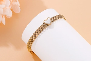 Detail of multi-layer gold steel bracelet featuring a white shell heart pendant inlay