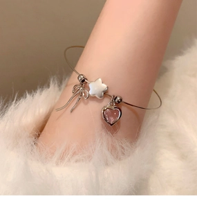 Detail of silver bangle with bow, star, and pink heart charms on a soft fabric background