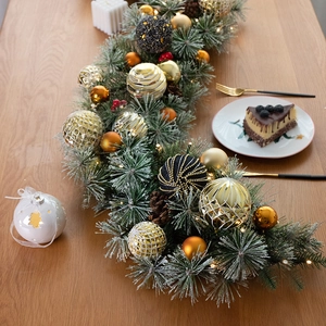 Lush Christmas pine garland with pinecones, ornaments and LED lights on a wooden table