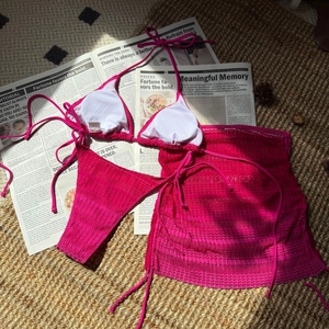 Flat lay of Fuchsia three-piece bikini set with mesh beach skirt and crochet texture