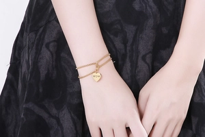 Close-up of golden double-layer pearl chain bracelet with MOM heart pendant on wrist