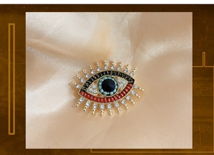 Macro shot of gold-plated evil eye brooch with blue beads and pearls on silk