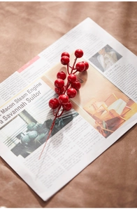 Detail of glossy red artificial Christmas berry stems on vintage newspaper background