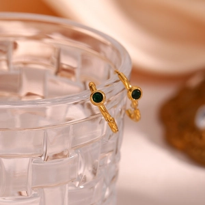Close-up of gold plated hoop earrings with green round zircon on a glass edge