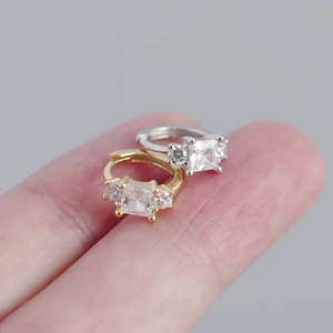 Close-up of square zircon hoop earrings in gold and silver held on a finger for scale